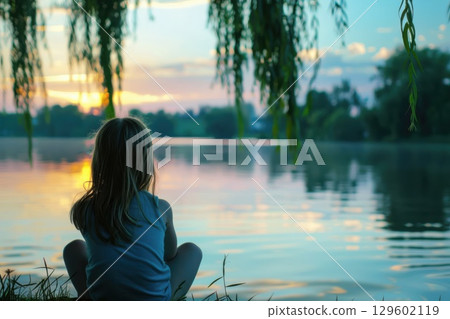 Young Girl  watching sunset by water, immersed in feelings of loneliness and calm reflection. 129602119