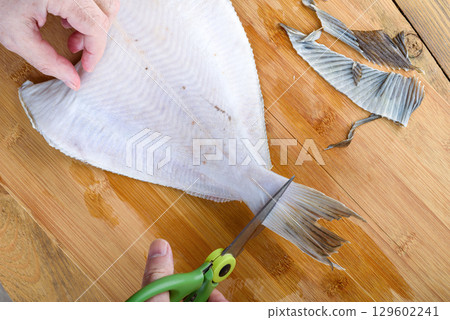 Cutting off flounder fins with kitchen scissors over a wooden cutting board. Cutting off flounder fins with kitchen scissors over a wooden cutting board. 129602241