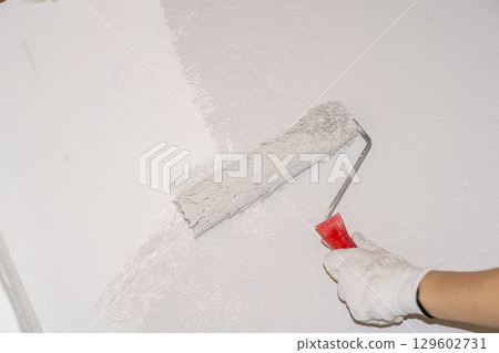 A woman manually paints a wall with a paint roller. Painting the apartment, renovation with white paint. A woman manually paints a wall with a paint roller. Painting the apartment, renovation with white paint. 129602731