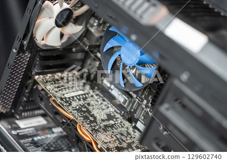 The interior of a desktop computer features a cooling fan, a graphics card, and various components in a tech-driven environment. 129602740