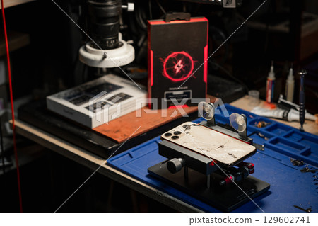 A technician examines a smartphone with a cracked screen in a bustling phone repair service environment. 129602741