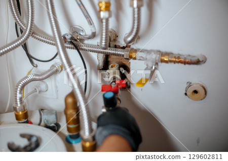 Gloved Hand Operating a Red Water Valve 129602811