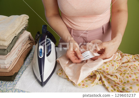 Woman inspecting garment label, ironing board behind Woman inspecting garment label, ironing board behind 129603237