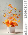 Crispy Potato Chips in Paper Bag with Colorful Seasoning Flying Against Light Background 129603947