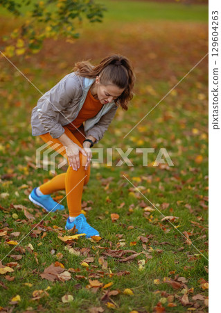unhappy modern woman in fitness clothes in park got leg injury 129604263
