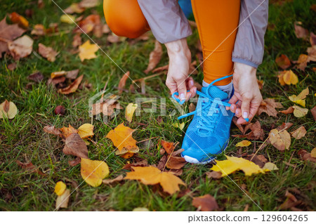 Stylish woman in fitness clothes in park tying shoelaces Stylish woman in fitness clothes in park tying shoelaces 129604265