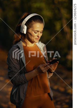 stylish woman in fitness clothes in park with headphones 129604275