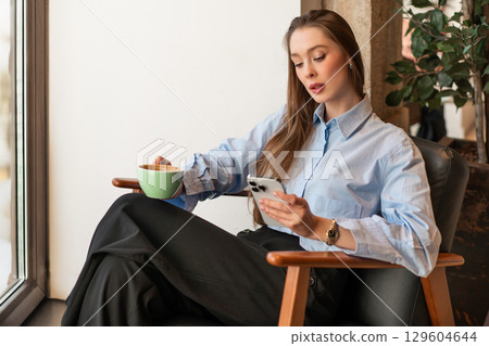Young woman sitting by window holding cup and 129604644