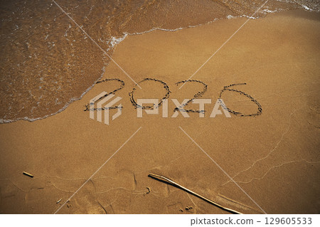 Imprint numbers 2026 of new year with oncoming wave on wet yellow sand on beach 129605533