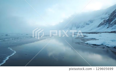 A picturesque beach featuring reflective waters and snow-dusted mountains in the distance, blending warmth and coolness 129605699