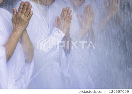 A middle-aged woman in a white robe undergoing waterfall training 129607099