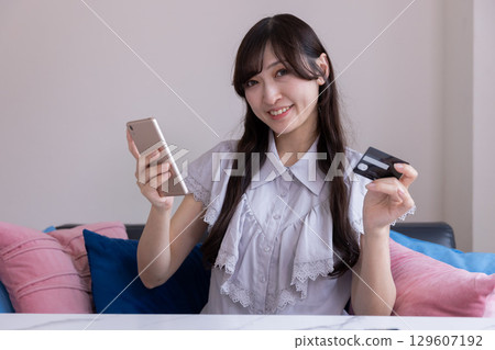 一位面帶微笑的日本女性正在用智慧型手機享受網路購物 一位面帶微笑的日本女性正在用智慧型手機享受網路購物 129607192