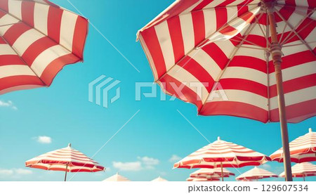 Red and white striped umbrellas arranged in a row on the beach, symbolizing summer fun and relaxation Red and white striped umbrellas arranged in a row on the beach, symbolizing summer fun and relaxation 129607534