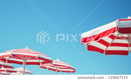 A vibrant display of red and white striped umbrellas at the beach, evoking a cheerful summer vacation vibe 129607535