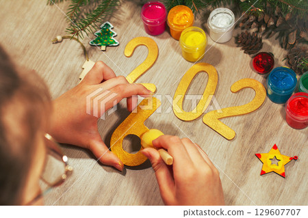 Children's hands paint yellow color wooden toy number six with spruce branches, pinecones and and other figures of new year on table Children's hands paint yellow color wooden toy number six with spruce branches, pinecones and and other figures of new year on table 129607707