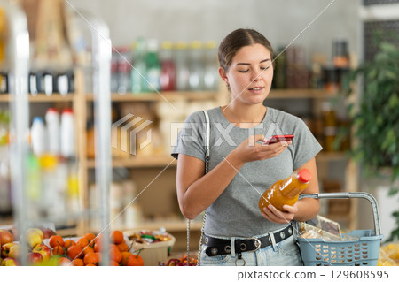 Girl scanning QR code on bottle peach juice label in grocery department of supermarket 129608595