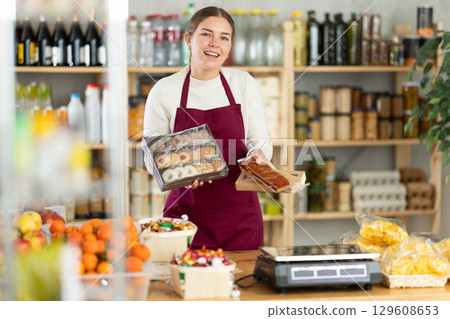 young saleswoman holds cookies and sweets in her hands. 129608653