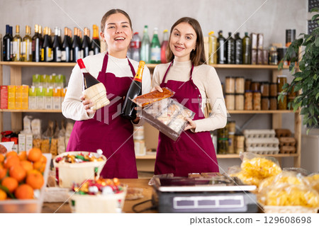 Young saleswomen are holding champagne, wine and sweets in their hands. Young saleswomen are holding champagne, wine and sweets in their hands. 129608698