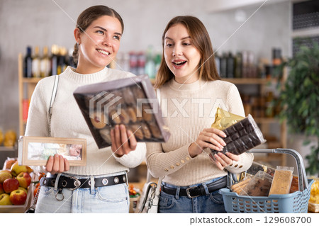 Two girls in store while shopping, choose sweets and chat sweetly Two girls in store while shopping, choose sweets and chat sweetly 129608700