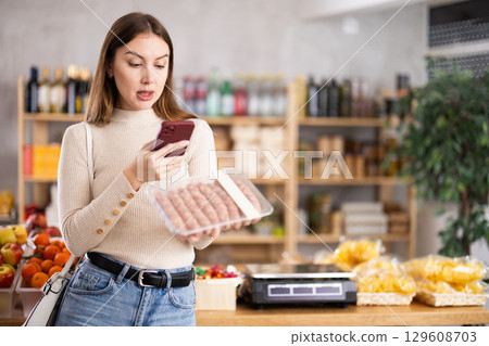Young woman scanning qr code of raw sausages Young woman scanning qr code of raw sausages 129608703