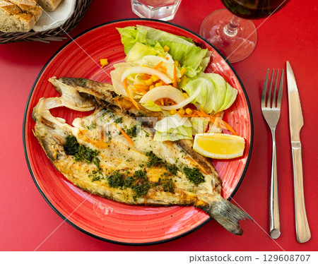 Grilled seabass with fresh salad and lemon on red plate 129608707