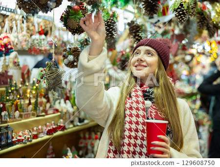 Young woman in souvenir shop examines Christmas handmade toys 129608750