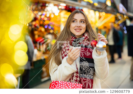 Smiling girl choosing Christmas tree balls and shopping at festive fair before Xmas Smiling girl choosing Christmas tree balls and shopping at festive fair before Xmas 129608779