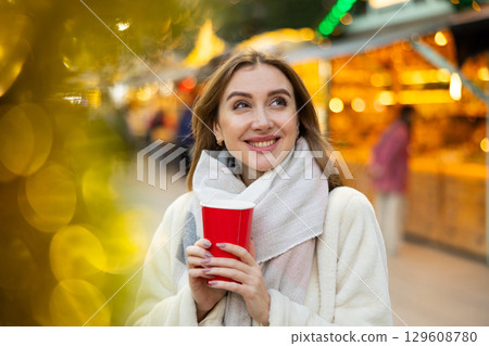 Young woman stands with glass of hot coffee in her hands and enjoys festive New Year atmosphere Young woman stands with glass of hot coffee in her hands and enjoys festive New Year atmosphere 129608780