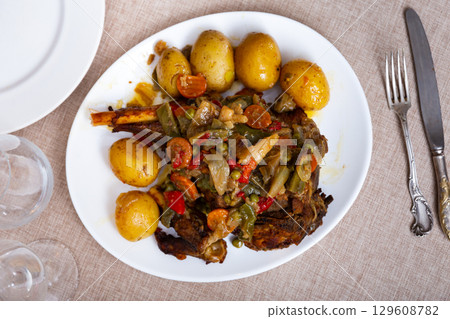 Mutton leg baked with vegetables served with side dish of boiled potatoes. Mutton leg baked with vegetables served with side dish of boiled potatoes. 129608782