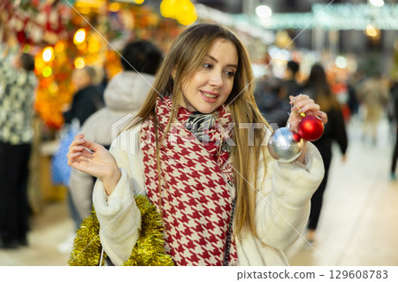 Young girl bought New Years balls toys and tinsel and in shopping pavilion and admires her purchase Young girl bought New Years balls toys and tinsel and in shopping pavilion and admires her purchase 129608783