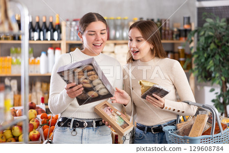 Two girls in store while shopping, choose sweets and chat sweetly Two girls in store while shopping, choose sweets and chat sweetly 129608784