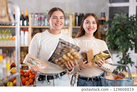 Two friends buy various sweets together - cookies and nougat in grocery supermarket 129608819