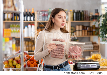 Girl looking at raw bbg sausage and raw pork chop in store 129608853