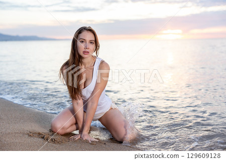 Girl sitting at sand at sea shore at sunset 129609128