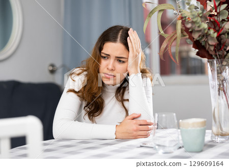 Upset woman sitting at table at home Upset woman sitting at table at home 129609164