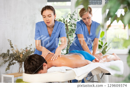 Two professional masseuses performing back massage for male patient 129609374