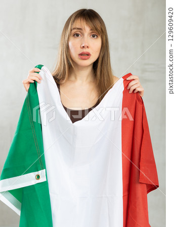 Sad young woman holding flag of Italy against unicoloured background 129609420