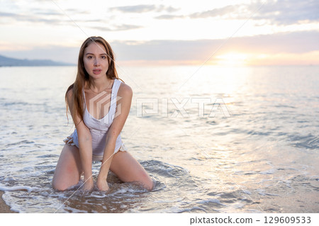 Young woman standing on knees on sand on beach, posing artistically Young woman standing on knees on sand on beach, posing artistically 129609533