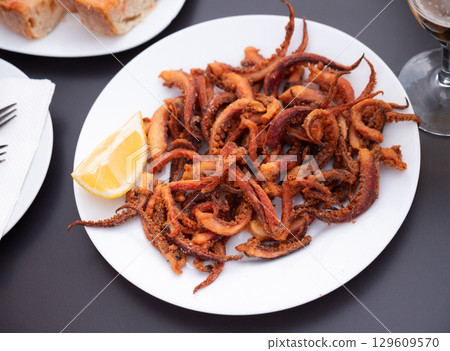 Fried tentacles squid served on white plate with potatoes, lemon slices 129609570