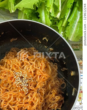 Bibimyeon, a flavorful Korean dish featuring cold noodles tossed in a spicy, tangy sauce, topped with fresh vegetables and a boiled egg. Perfect for summer meals, showcasing vibrant flavors and colors 129612244
