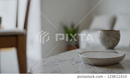 Stylish ceramic cup and saucer slowly spin on a beautiful marble coffee table, showcasing elegant tableware in a contemporary living room setting 129612810