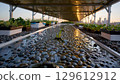 Gentle water cascading over smooth pebbles in rooftop garden, reflecting sustainable urban agriculture during soft sunset light with serene cityscape backdrop 129612912