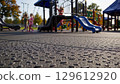 Tiny, glistening water droplets rest on the textured surface of a playground safety mat, while children enjoy the playground equipment in the background 129612920