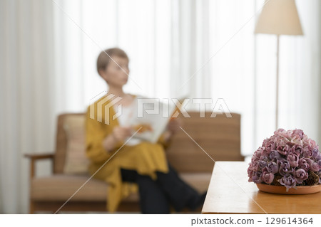 Senior woman reading a book on the sofa in the living room Senior woman reading a book on the sofa in the living room 129614364