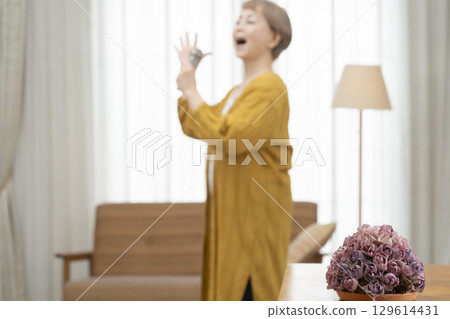 老年婦女在客廳沙發上唱卡拉 OK 作為愛好 129614431