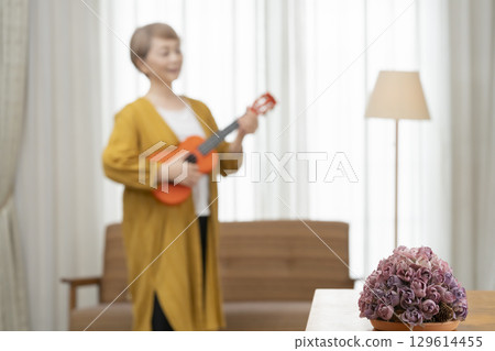 Senior woman playing the ukulele as a hobby on the sofa in the living room Senior woman playing the ukulele as a hobby on the sofa in the living room 129614455