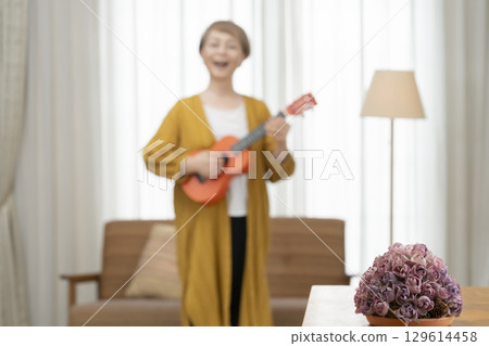 Senior woman playing the ukulele as a hobby on the sofa in the living room 129614458
