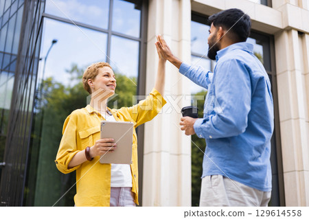 A woman and a man high-fiving in front of a modern building, success and teamwork. A woman and a man high-fiving in front of a modern building, success and teamwork. 129614558