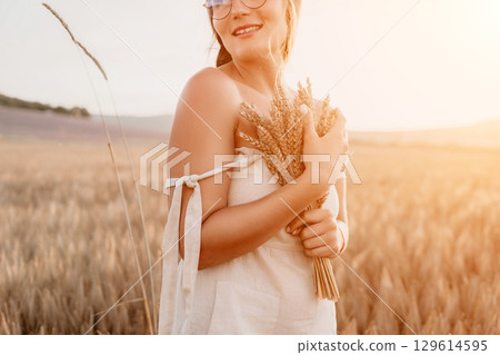Woman wheat field. Agronomist, Woman farmer check golden ripe barley spikes in cultivated field. A woman is holding a bunch of wheat in her arms. Woman wheat field. Agronomist, Woman farmer check golden ripe barley spikes in cultivated field. A woman is holding a bunch of wheat in her arms. 129614595
