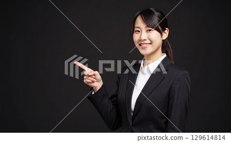 一位微笑的女商務人士在黑色背景下用雙手指向一側 129614814
